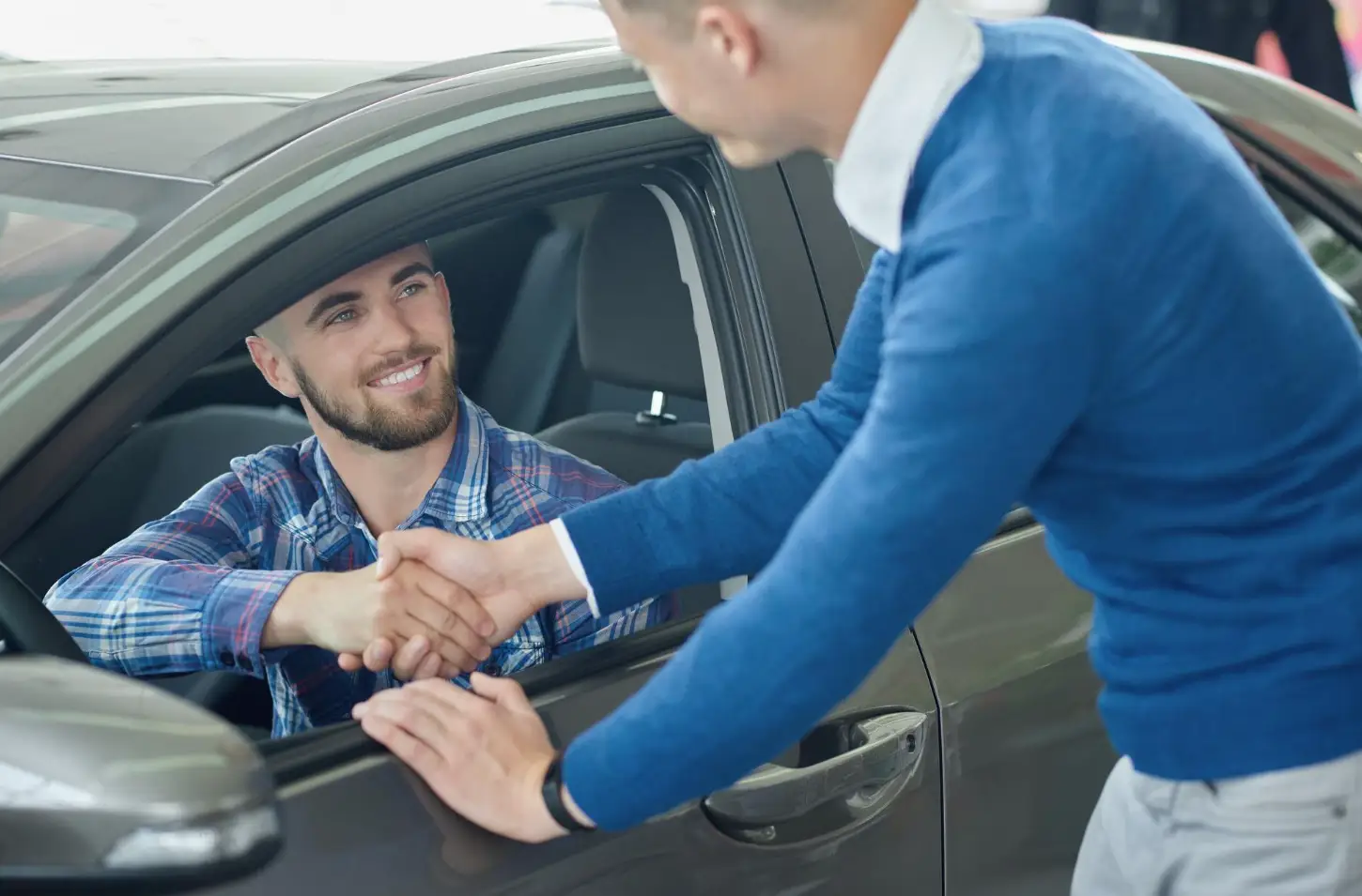 El dueño estrecha la mano del comprador desde la ventana de su auto.