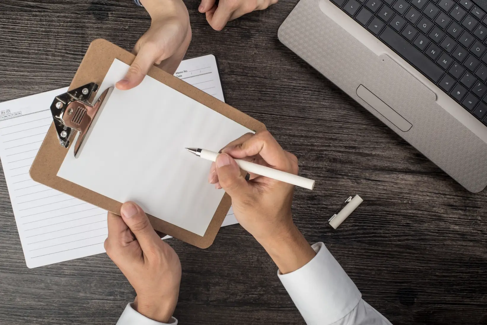 Dos personas firman documentos sobre un escritorio.